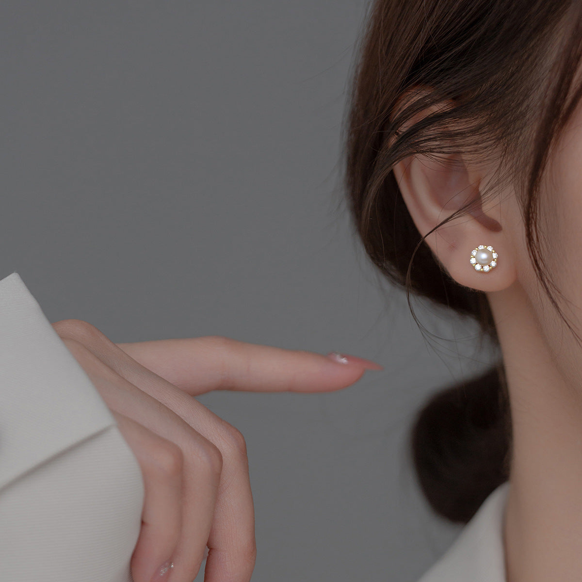 Woman wearing Pearl and Cubic Zirconia Stud Earrings with a white pearl center surrounded by sparkling stones in a gold-plated setting.