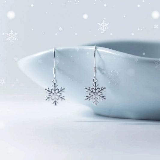 a pair of sterling silver snowflake drop earrings hanging on a blue bowl